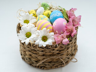 Obraz na płótnie Canvas Easter gift. Natural decoration. Handmade holiday composition. Colorful painted eggs with creative design Spring white pink flowers in basket with straw isolated on white background.
