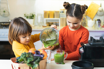 Children pour and eating green smoothies from blender in the kitchen. Funny Brother and Sister Make...