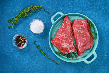 Raw steak on a cutting board with rosemary and spices, blue background, top view. Fresh grilled meat. Grilled beef steak.