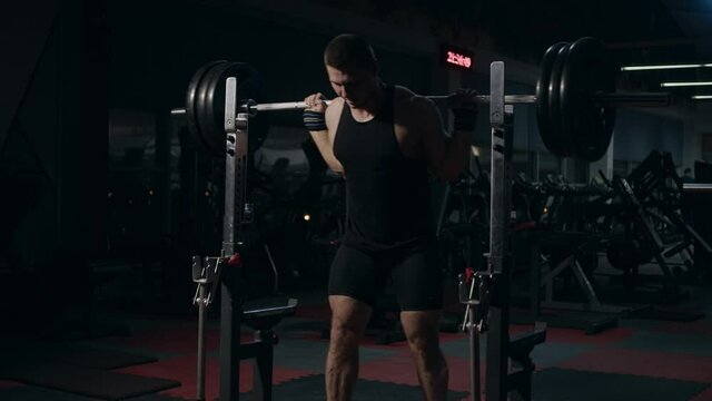 Young powerlifter shirtless doing compound movement in gym. Squat