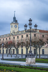 Fototapeta premium Plaza de Cervantes in the historic center of Alcalá de Henares. Detail of a street lamp in the foreground, and town hall tower in the background, on a winter morning. Vertical view.