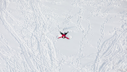 Minimalist photo concept - Happy young woman in red lying on snow and making snow angel figure