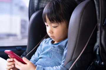 チャイルドシートに座りスマートフォンを見る日本人の女の子