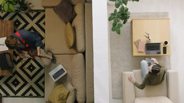 Top view shot of young man loudly playing electric guitar in his apartment while his female neighbor trying to work on laptop. She is knocking on wall and complaining about noise