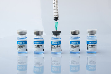Taking the liquid vaccine from bottle with a syringe  among other Covid-19 vaccine bottles