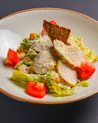 Caesar Salad served in a white plate over black background. One plate of salad for healthy and full dinner.