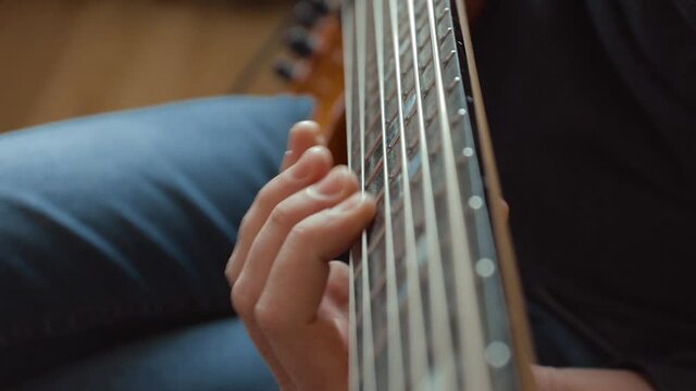 The musician rehearses at home on a six-string bass guitar. Close-up. Soft Focus