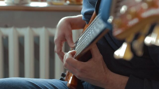 The musician rehearses at home on a six-string bass guitar. Close-up. Soft Focus
