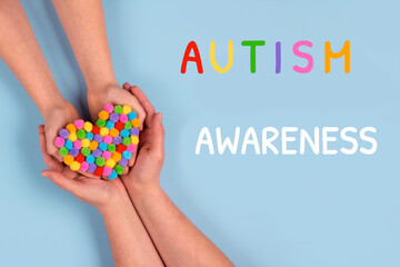 World Autism Awareness Day concept - autistic child's hands supported by mother holding multicolored heart on blue background. Autism spectrum disorder and child mental health concept. Selective focus