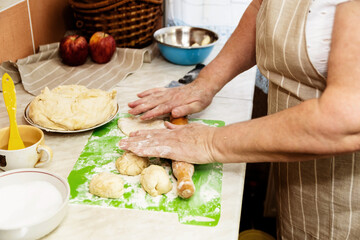 An elderly woman prepares pies from the dough. Close-up hands hold a rolling pin.