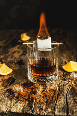Glass of whiskey on a wooden background with fire on marshmallows