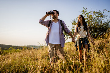 Happy couple is hiking in mountain. They are watching nature with binoculars.
