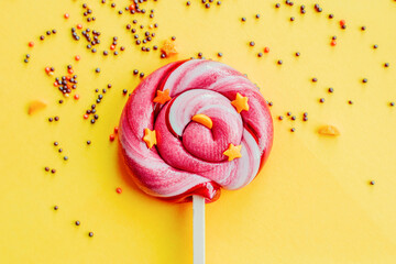 Colorful lollipop with sugar topping isolated over yellow paper background. Flat lay. Copy space....