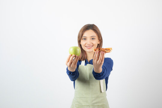 Image of woman in apron trying to choose what to eat apple or pizza
