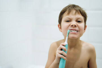 portrait of cute 6 years old boy brushing teeth with electic brush in bathroom. Image with selective focus