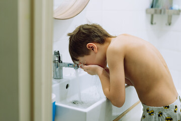 cute 6 years old boy washing his face over the sink in bathroom. Image with selective focus