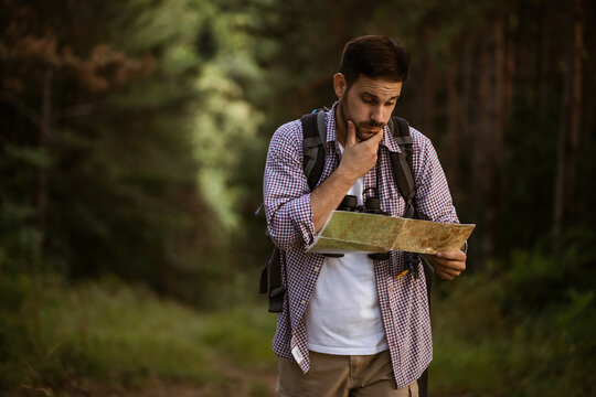 Adult man is hiking in forest. He is looking at map.