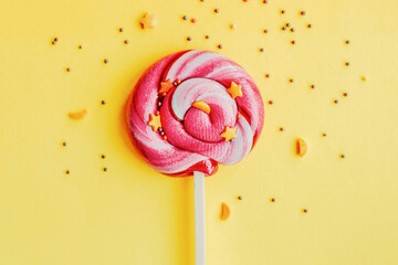 Colorful lollipop with sugar topping isolated over yellow paper background. Flat lay. Copy space. Minimal concept. Close up