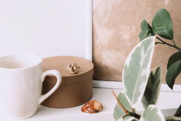 Obraz na płótnie Canvas Still life. Cup of coffee, blank beige poster frame, craft round box and indoor evergreen potted plant on the white wall. Home office