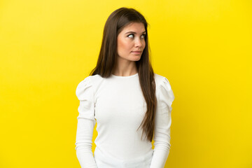 Young caucasian woman isolated on yellow background making doubts gesture looking side
