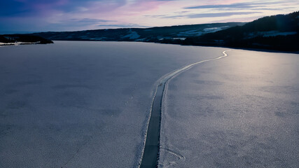 Ice skating road on the clear glassy ice of a large frozen lake with light snow on top of the ice.