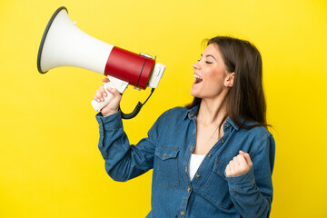Young caucasian woman isolated on yellow background shouting through a megaphone to announce...