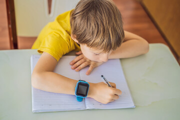Little boy sitting at the table and looking smart watch. Smart watch for baby safety. The child...