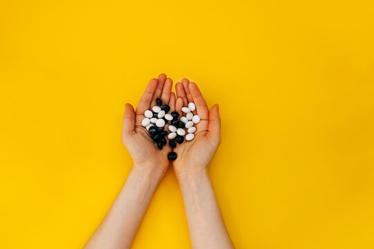 Female hands holding bunch of candies, peanuts in chocolate, on yellow background.