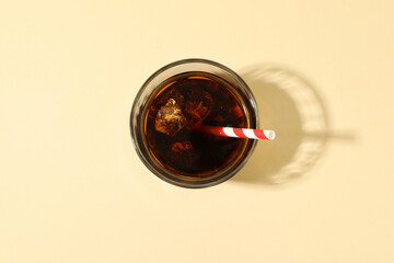 Glass of cola with ice cubes and straw on beige background