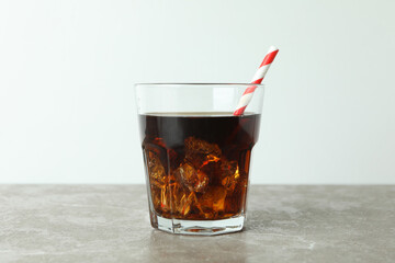Glass of cola with ice cubes and straw on gray table