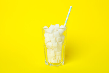 Glass with sugar cubes and straw on yellow background