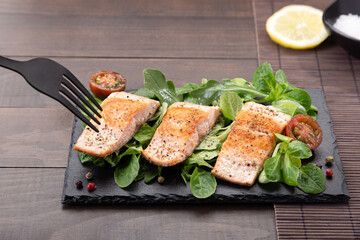 fork pricking Salmon fillets on slate dish on wooden table background.