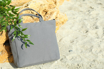Stylish eco bag and twig outdoor on beach, space for text