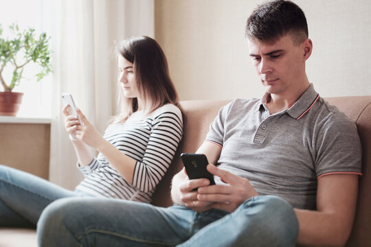 Offended young people are sitting at home on the couch and looking at the phone - A couple quarreled and sit separately - A ruined relationship between a man and a woman - Quarantine lifestyle