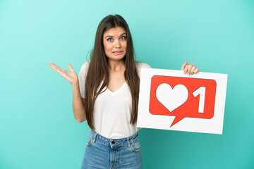 Young caucasian woman isolated on blue background holding a placard with Like icon with surprised expression