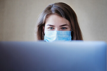 Young woman in a mask from covid at the workplace with a laptop with a focus on the computer...