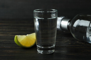 Bottle of vodka, shot and lime slice on wooden background