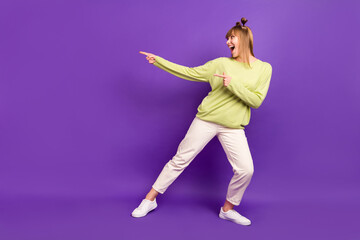 Fototapeta na wymiar Photo of charming cute young woman dressed green pullover dancing looking pointing fingers empty space isolated purple color background