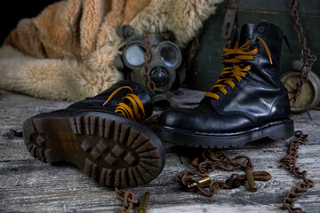 Leather boots with rusted chains and bullet shells with military gas mask and fur coat in background resting on wooden table