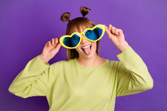 Photo of adorable childish young lady wear green sweater arms dark heart eyewear showing tongue isolated violet color background