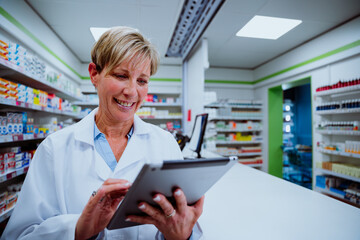 Caucasian female pharmacist scrolling through digital tablet standing besides counter in pharmacy 