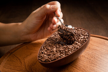 Hand sticking a metallic spoon in a stuffed chocolate easter egg with grated chocolate on the top...