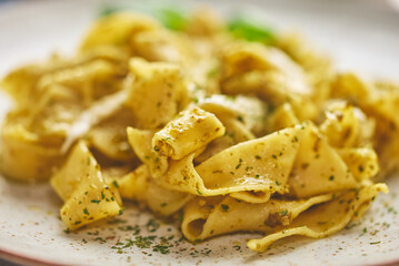 Close up of fresh cooked tagliatelle pasta with green pesto and herbs