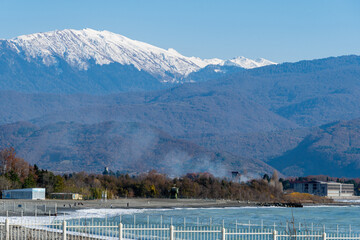 Sochi, Russia - December 8, 2020: Border with Abkhazia in background of mountains with snowy peaks. Neutral strip is fenced on both sides. On seashore in neutral zone, fishermen catch fish.