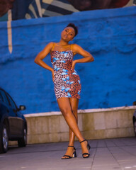 Fashionable urban style with an African girl on a city street at night. short colorful leopard dress
