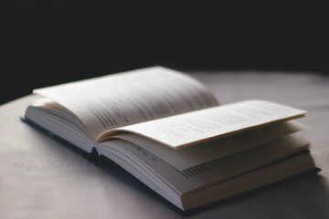 Side view of open book lies on table with white tablecloth on black background. Soft light
