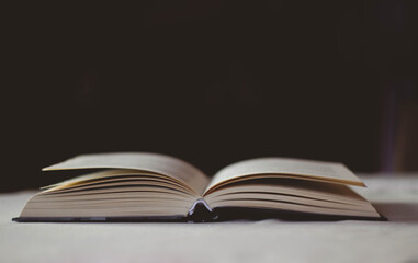 Open book lying on a table with a white tablecloth on a black background. 
