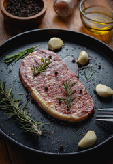 Raw fresh beef steak with olive oil, Colorful pepper, garlic and the rosemary leaf fresh on in the black tray on the wooden table, Top view.