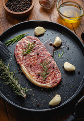 Raw fresh beef steak with olive oil, Colorful pepper, garlic and the rosemary leaf fresh on in the black tray on the wooden table, Top view.