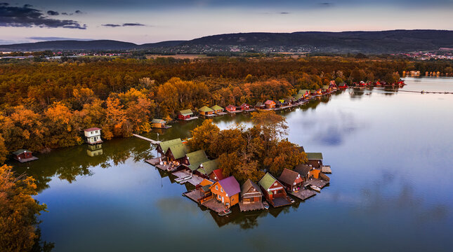 Tata, Hungary - Beautiful autumn sunset over wooden fishing cottages on a small island at Lake Derito (Derito-to) in October with clear blue sky and autumn foliage. Aerial panoramic view